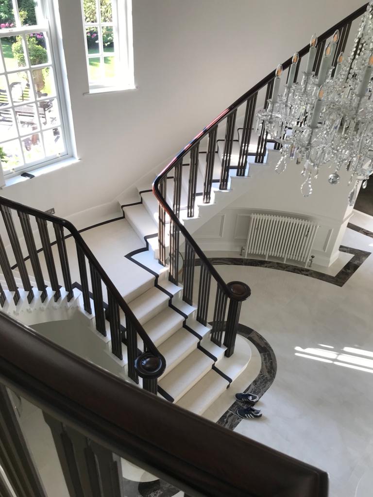 A pristine white stair runner with dark border fitted on a grand curved staircase — recent work by Lewis's Concept Carpets