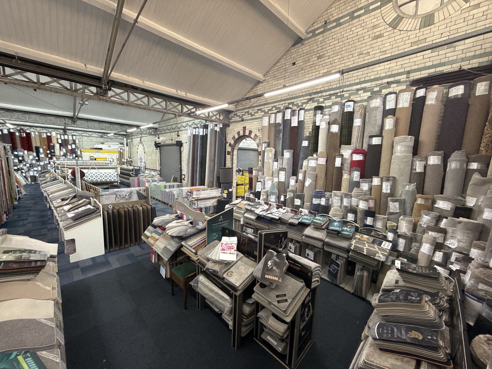Inside the Lewis's Concept Carpets showroom in Longsight — rolls of carpet and flooring samples under a Victorian tiled arch